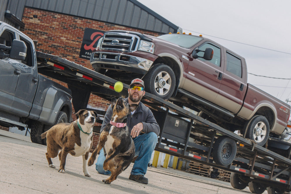 A customer with his dogs in front of a car hauler loaded with trucks